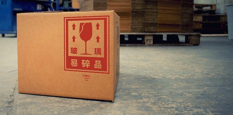 Diseño bōlí sobre una caja en primer plano, a modo de advertencia, en un almacén, donde se ven cajas y palés. Fotografía en color.