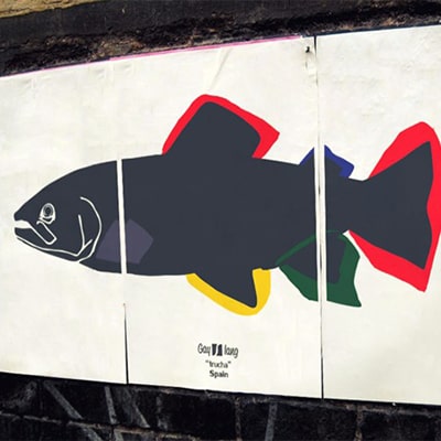 Fotografía en color de un póster con el diseño Trucha pegado en una pared de la calle.