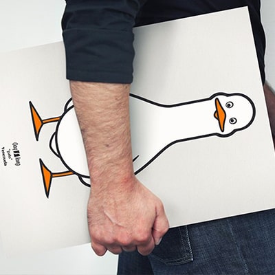 Fotografía en color de un primer plano de un póster con el diseño pato, el poste lo lleva un hombre bajo el brazo.