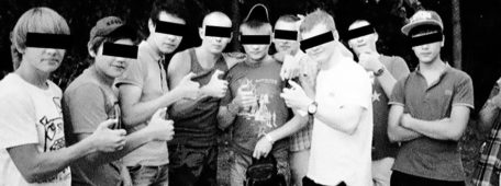 Miembros de Okkupay Pedofilyay, con su característico signo realizado con la mano, el signo OK pero doblando el pulgar. Foto en blanco y negro con una franja negra añadida tapando los ojos.