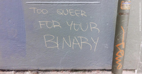 Graffiti with text Too Queer for your binary, on lilac wall with a down pipe.