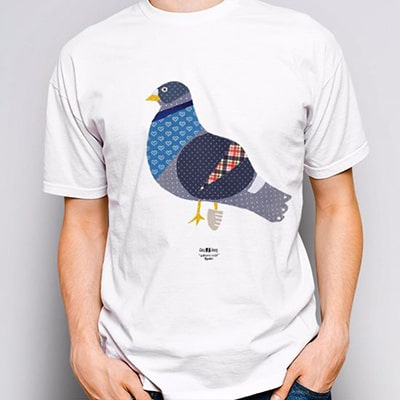 Close-up photograph of a white T-shirt worn by a boy with the Palomo Cojo drawing, a pigeon with a leg in plaster.