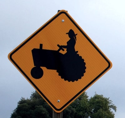 Señal de tráfico con una mujer en un tractor, que podría considerarse una virago.
