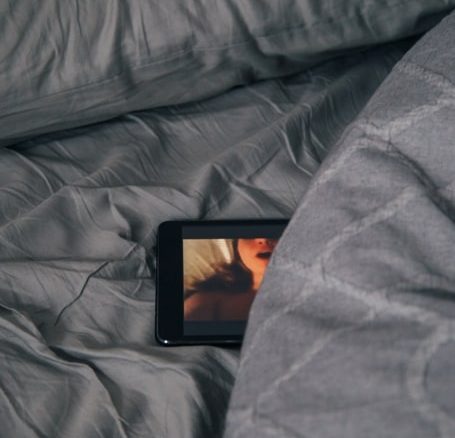 Un teléfono sobre la cama, en el que se ve una imagen pornográfica. La pornografía forma parte de la identidad sexual de millones de personas